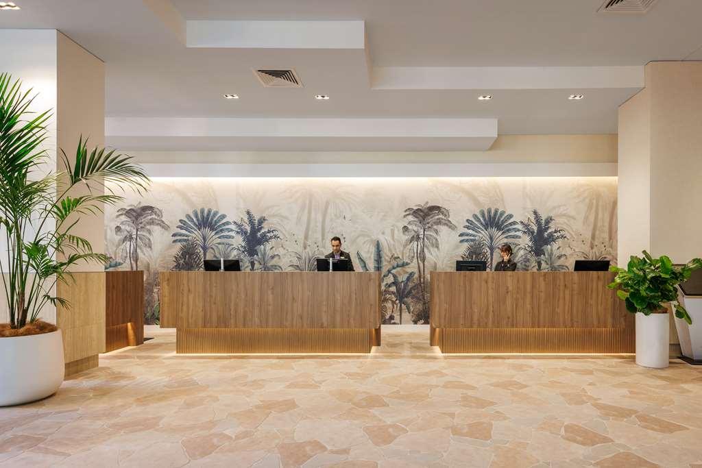 Amora Hotel Brisbane Interiør bilde The photo shows a modern reception area with two wooden reception desks. Behind the desks, there is a decorative wall featuring a large mural of tropical plants and palm trees, creating a serene atmosphere. The space is well-lit with overhead lights,
